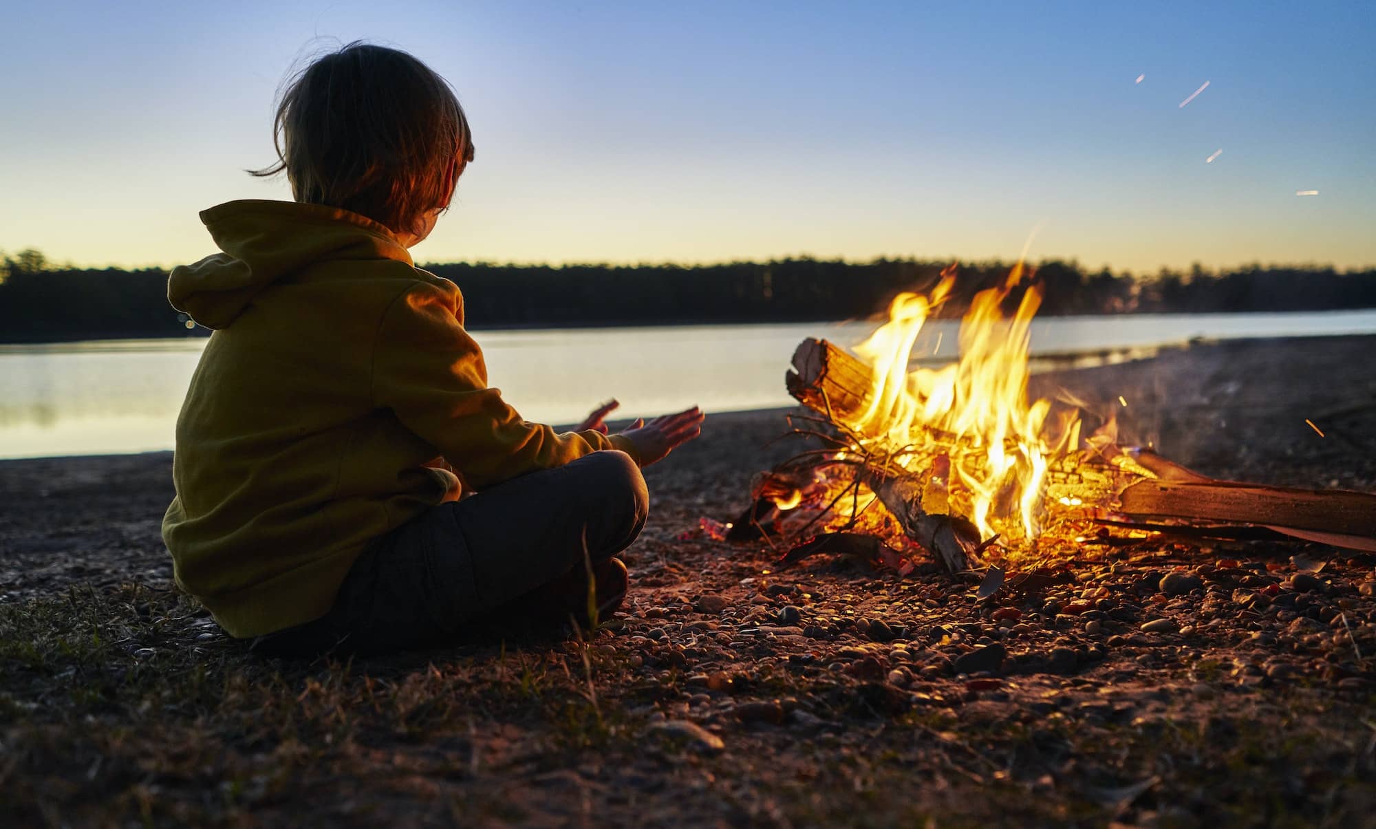Argentina, Patagonia, Concordia, boy sitting at camp fire at a lake